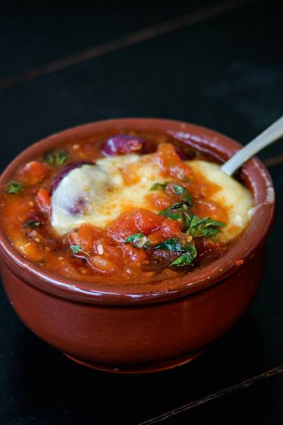 Polenta do padre, servida na cumbuca coberta por molho de tomate, azeitona preta e manjericão