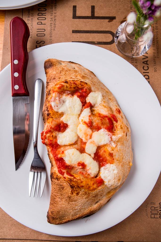 Fechado como um pastelão, o calzone leva recheio de presunto, mussarela, tomate e creme de alcachofra Fechado como um pastelão, o calzone leva recheio de presunto, mussarela, tomate e creme de alcachofra
