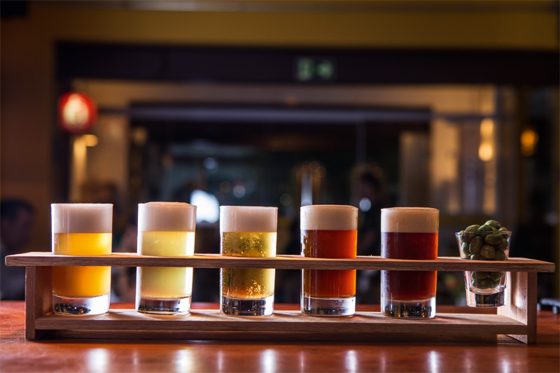 Para a degustação de cinco chopes chega à mesa copinhos de 100 mililitros, enfileirados num suporte de madeira Para a degustação de cinco chopes chega à mesa copinhos de 100 mililitros, enfileirados num suporte de madeira