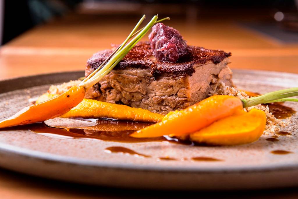 O leitãozinho tem carne macia sob pele crocante e a companhia de purê de cenoura O leitãozinho tem carne macia sob pele crocante e a companhia de purê de cenoura