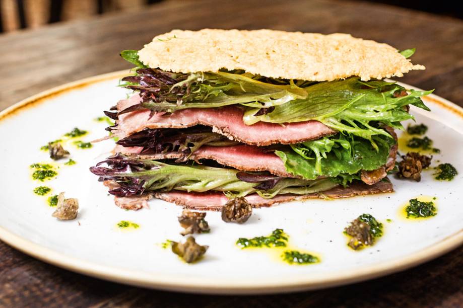 Salada de folhas intercaladas por rosbife e uma tela de pão crocante