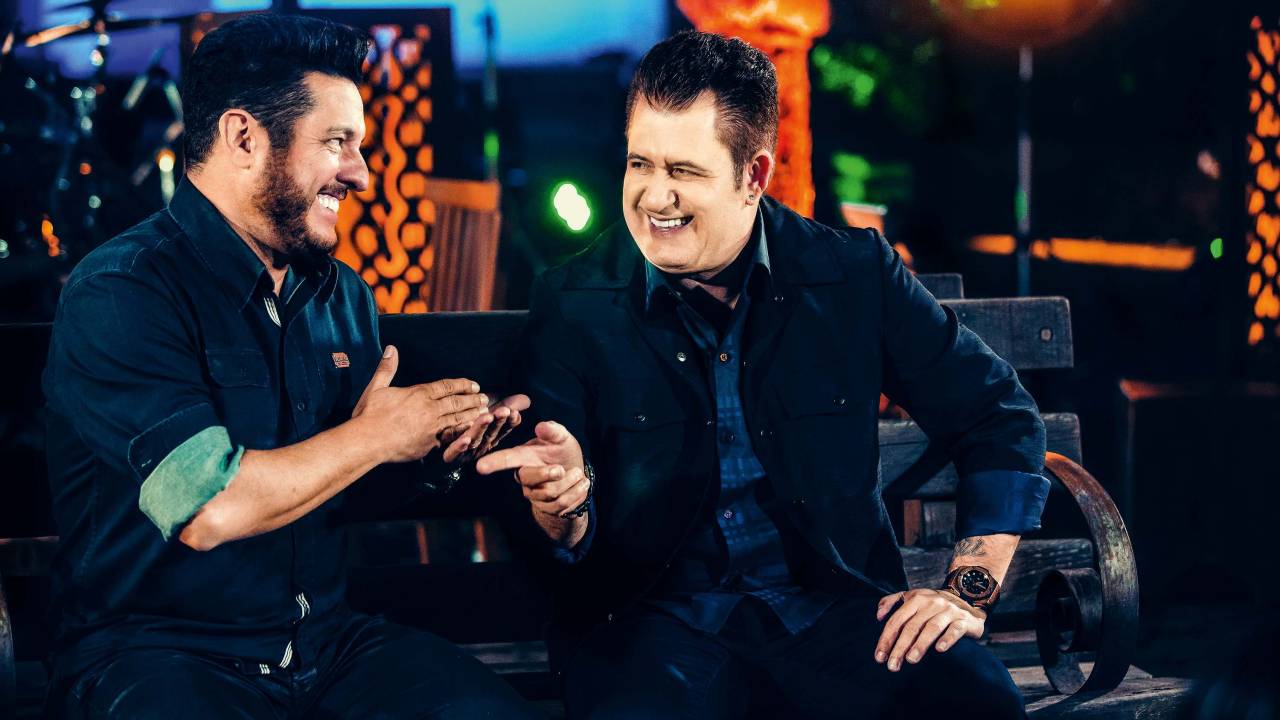 Dois cantores sertanejos sentados no palco