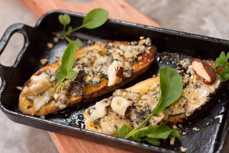 Bruschetta de queijo azul, mel, castanhas e minirrúcula: direto do forno a lenha