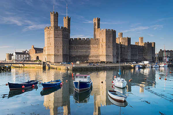 Boats moored at high tide in the harbour below Caernarfon Castle.