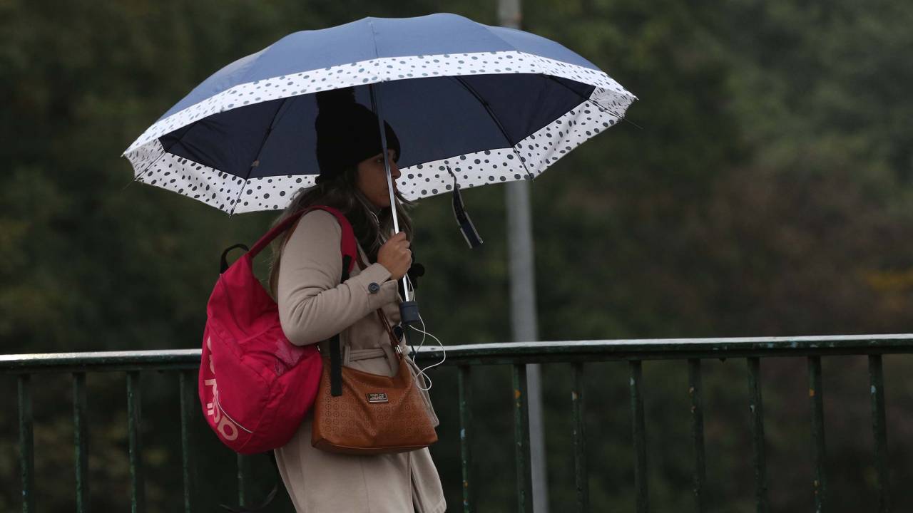 A imagem mostra uma mulher agasalhada e com guarda-chuva pelas ruas de São Paulo