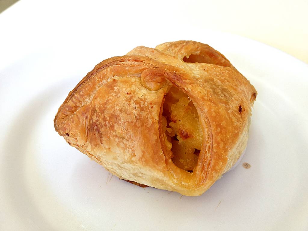 Taça de vidro com sorvete sobre base redonda de madeira, com pedaço de goiabada, pedaço de queijo e pequena faca ao lado, sobre mesa de madeira branca