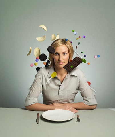 Unhealthy snacks floating around head of woman sitting in front of empty plate