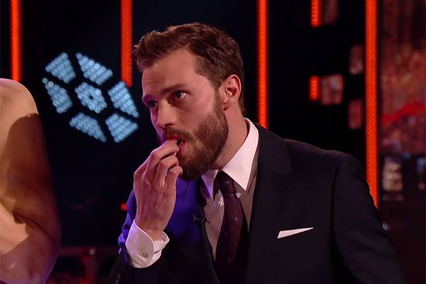 Jamie Dornan come pedaço de um bolo em tamanho real de Christian Grey. Assista à cena