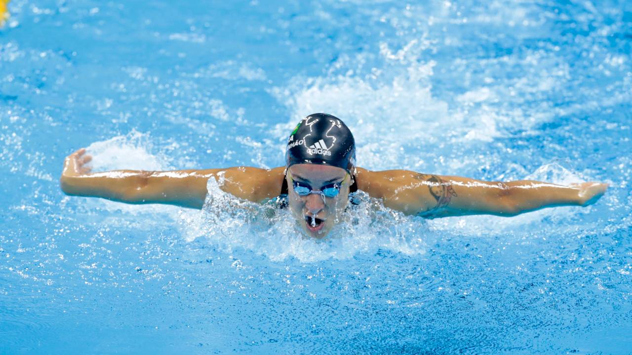 A foto mostra um atleta nadando em piscina durante competição