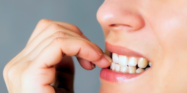 nervous young woman biting her nails on gray background