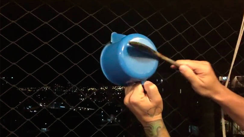 Imagem de uma mão segurando uma colher de pau e batendo uma em uma pequena panela azul
