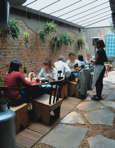 sofa-cafe2.jpeg MEsas em jardim com atendente em pé e clientes sentados