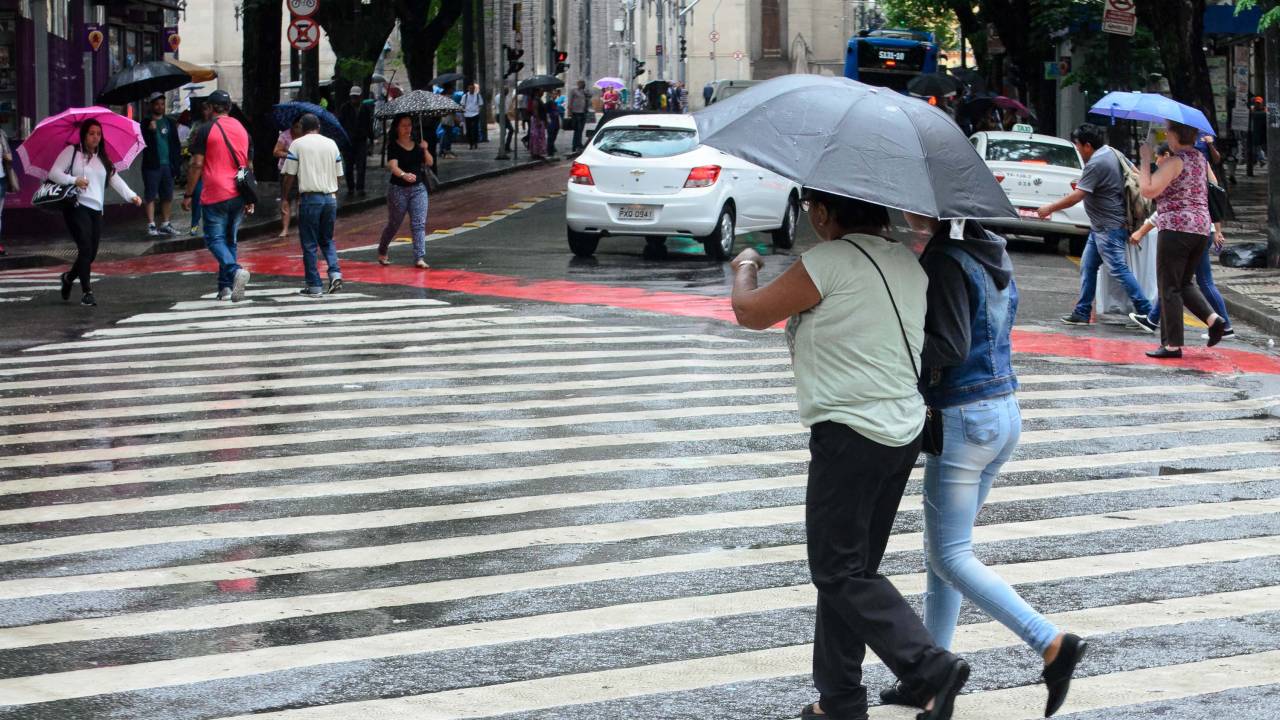 Imagem mostra pessoas em guarda-chuvas andando na rua