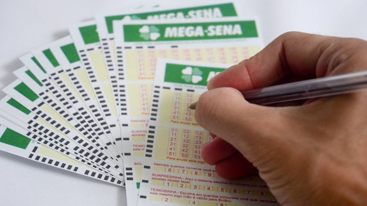 Imagem de uma mão preenchendo uma cartela da Mega-sena
