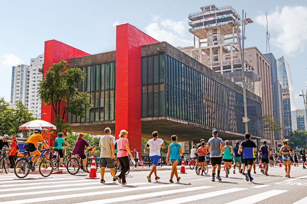 Foto mostra edifício do Masp, com pessoas andando na Avenida Paulista fechada em primeiro plano