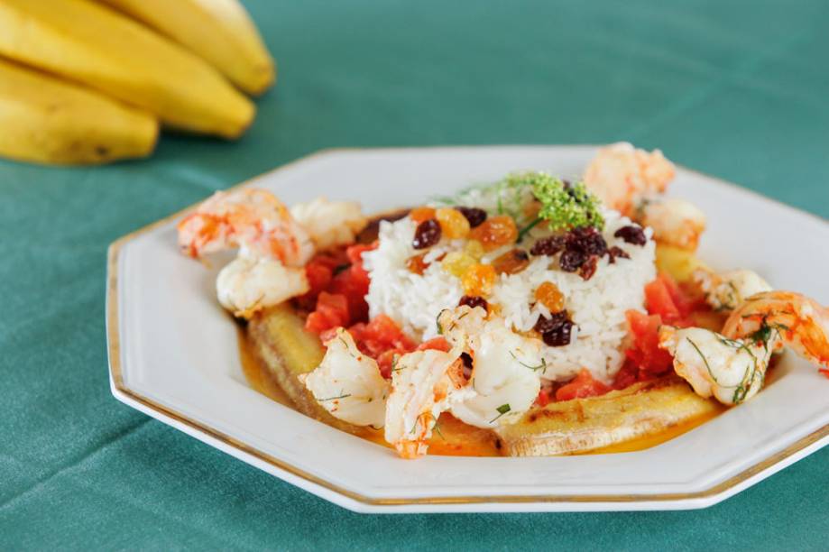 Camarão com tomate e banana flambado em aguardente da fruta ao lado de arroz com passas