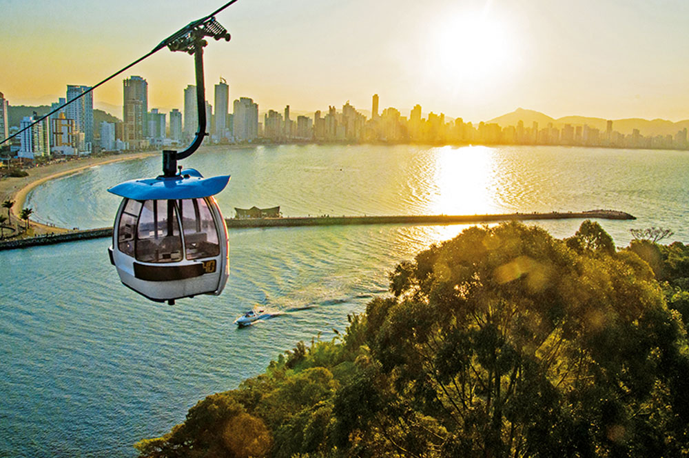 Pôr do sol e teleférico no Parque Unipraias, com a cidade ao fundo.