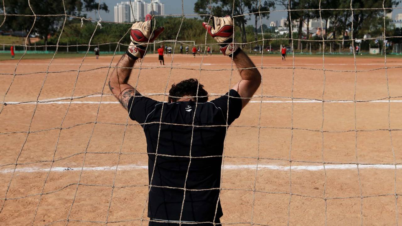 Imagem mostra goleiro com mãos erguidas em um campo de várzea