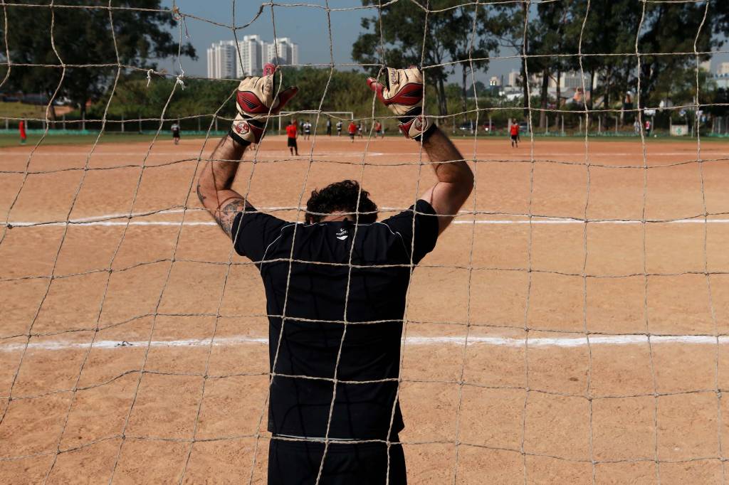 Imagem mostra goleiro com mãos erguidas em um campo de várzea