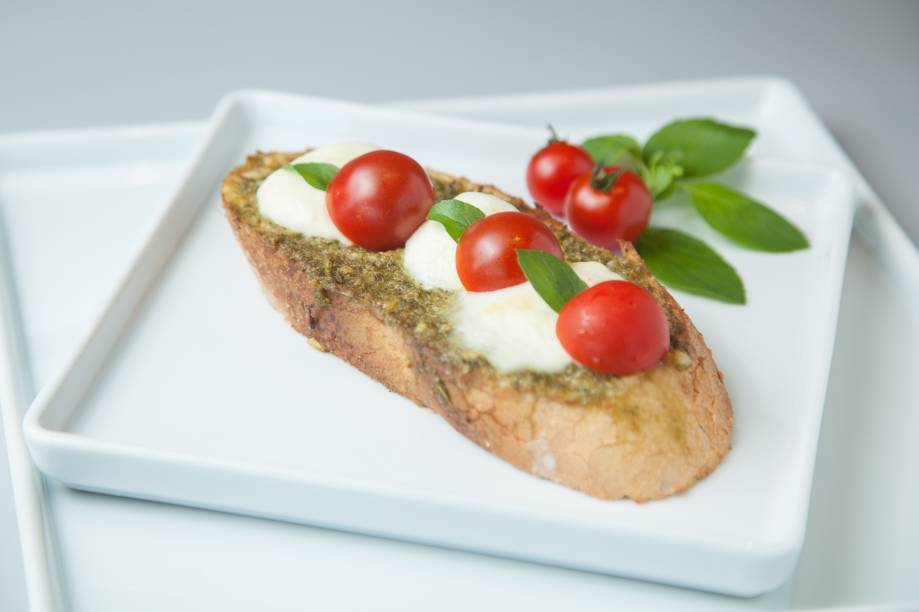 Tostada no filão italiano coberta por alho, molho pesto, tomate-cereja, mussarela de búfala e manjericão