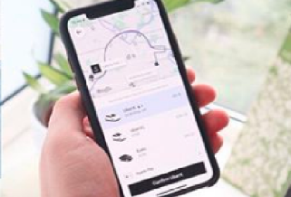 Uma mão segurando um celular. Na tela do equipamento aparece a interface do aplicativo da Uber, com a solicitação de uma viagem