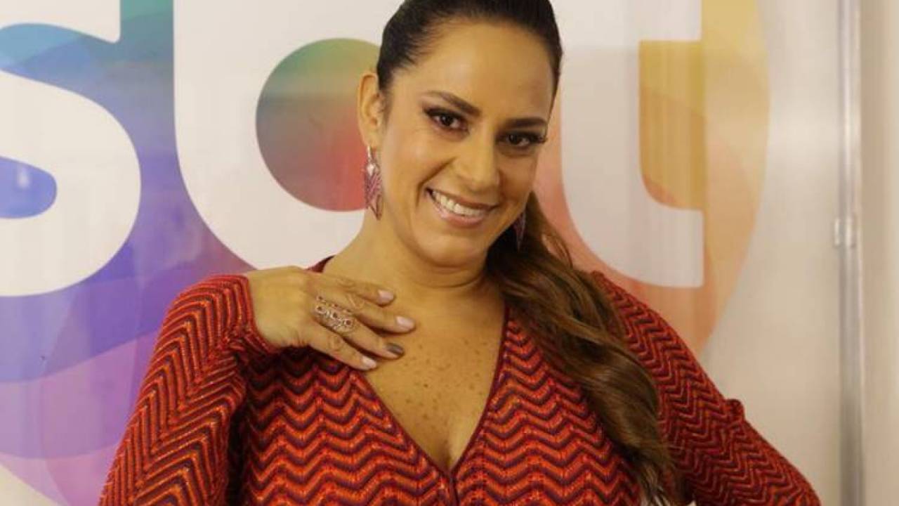 Silvia Abravanel posa sorrindo para a câmera atrás do logo do SBT