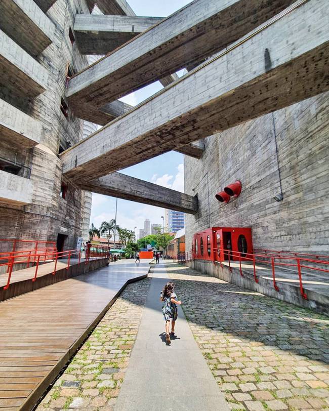 conexões suspensas entre os prédios do sesc pompeia. espaço entre eles é amplo e de passagem, tem uma menina andando