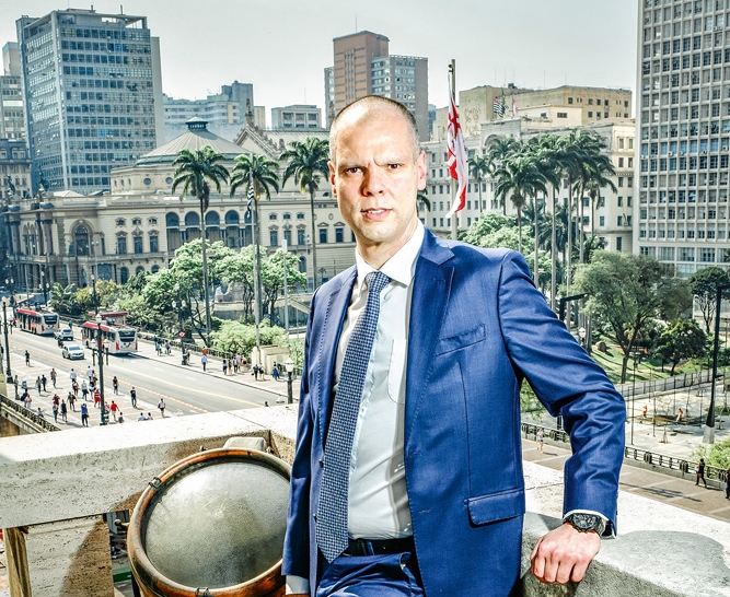 Imagem de Bruno Covas posando para foto com a cidade de SP ao fundo