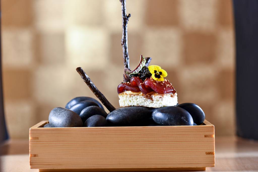 COMER & BEBER 2021 – Ryo Fatias de atum marinado sobre uma torrada de brioche, maionese de peixe e caviar, em cima de pedras pretas dentro de caixa de madeira.