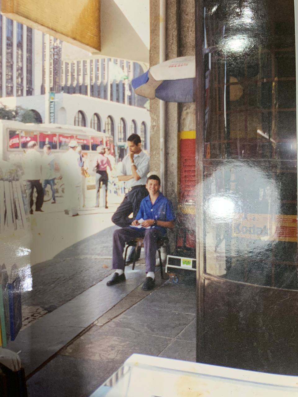 Thiago Landes (ARQUIVO PESSOAL) Foto antiga mostra Thiago Landes em ponto de engraxate na Avenida Paulista: de Franco da Rocha, paulista exibia sapatos lustrados e revistas masculinas para atrair mais clientes na calçada.