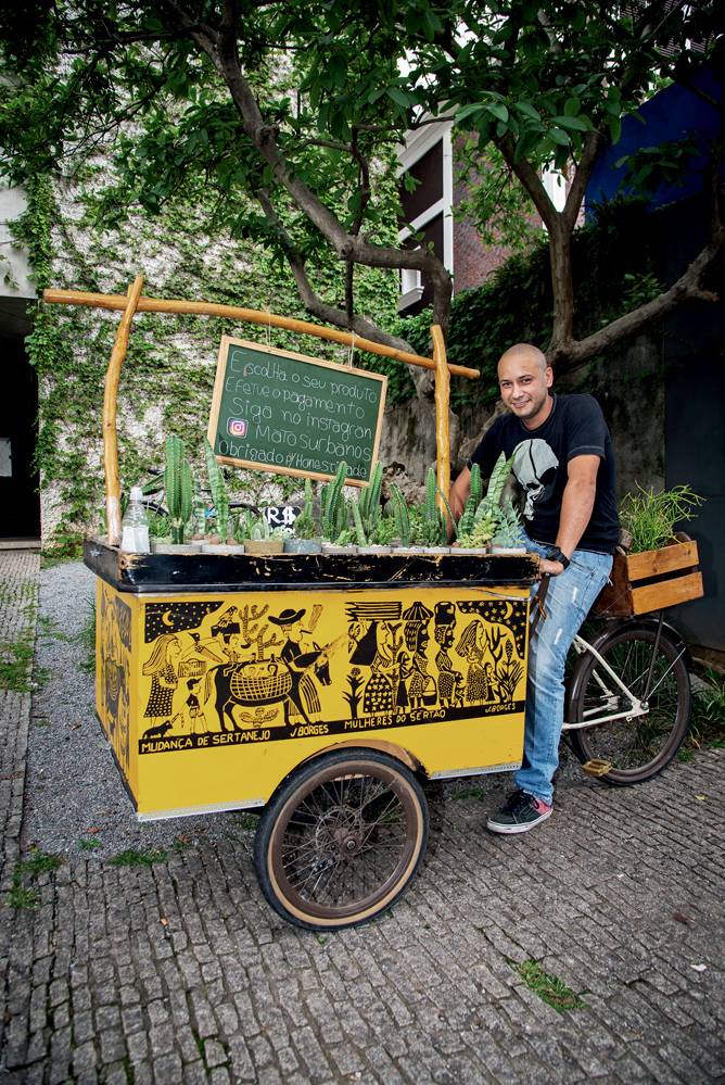Renato-Israel Joaquim Santana- Matos Urbanos (Rogério Pallatta) Israel Joaquim posa sentado em bicicleta com bancada amarela, mini-lousa com nome