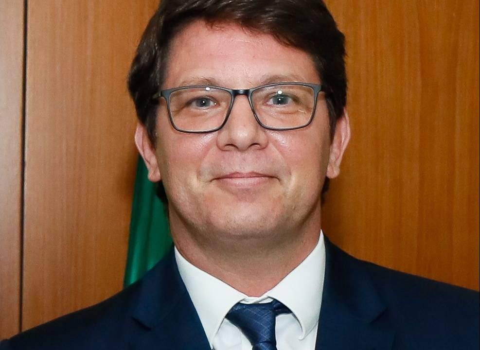 Imagem mostra Mario Frias usando óculos e de terno, sorrindo para câmera