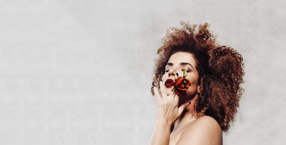 Vanessa da Mata, de olhos fechados, levando uma rosa com a mão esquerda a boca