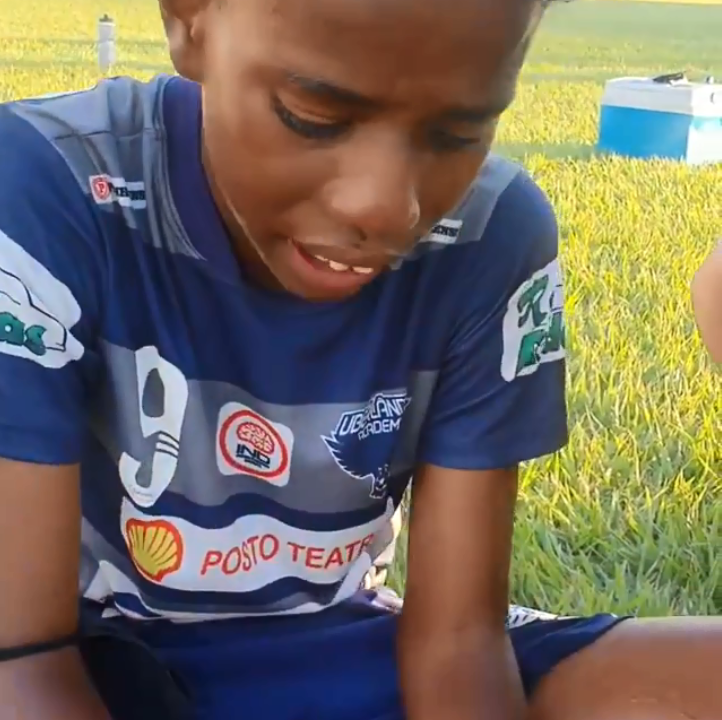 Menino de 11 anos, uniformizado, chorando em um campo de futebol