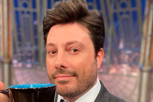 Imagem mostra Danilo Gentili segurando caneca no cenário do seu programa do SBT, o 'The Noite'