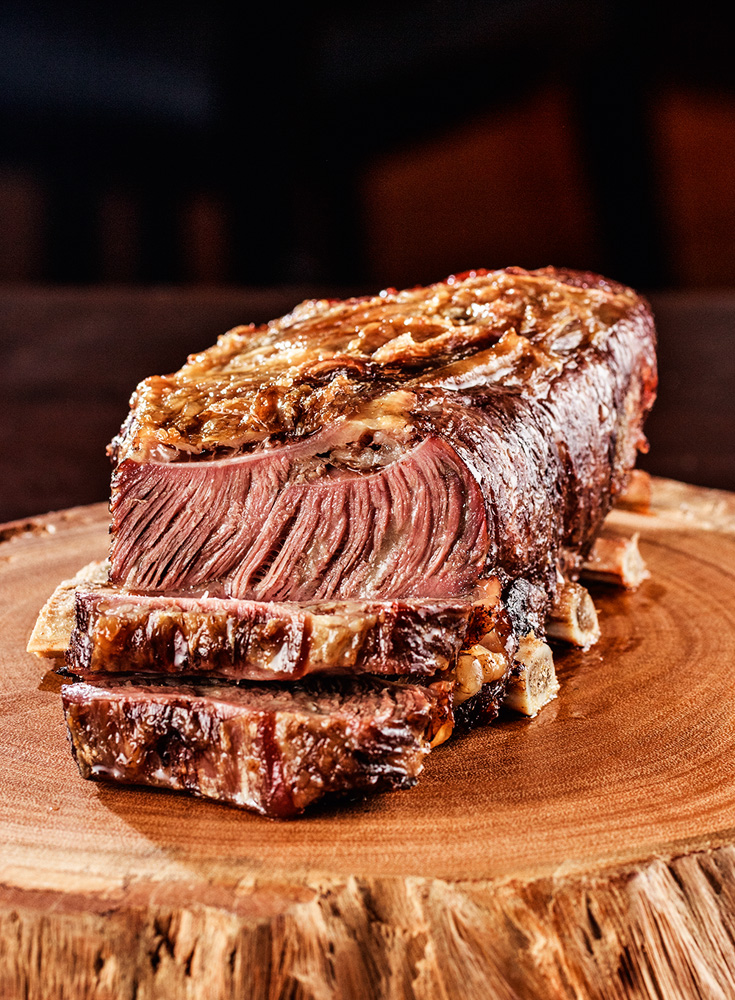 Costela Gaúcha – NB Steak Costela gaúcha cortada em fatias, sobre tábua redonda de madeira para churrasco