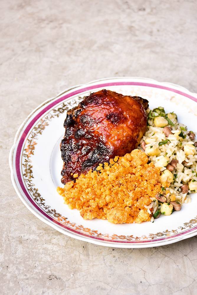 Frango com baião de dois e farofa – Fitó Frango marinado na cachaça, acompanhado de baião de dois e farofa em um prato branco decorado na borda