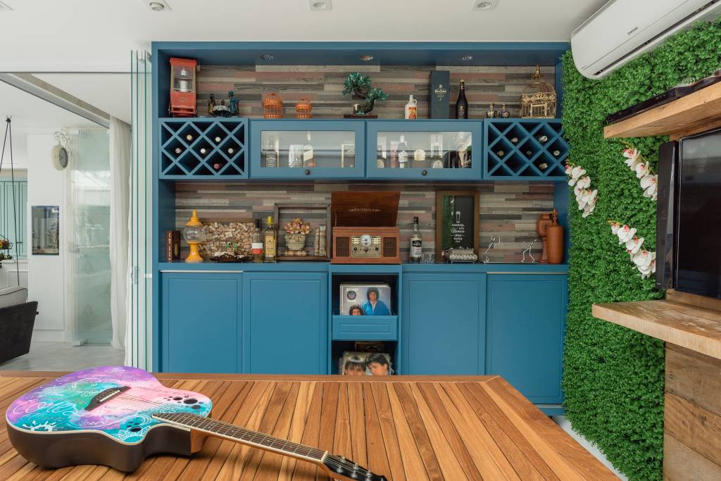 Reforma Marcos (Divulgação) (1) Móveis na cor azul e mesa de madeira de demolição ocupam espaço da casa reformada do músico Marcos. Na mesa, aparece uma guitarra colorida.