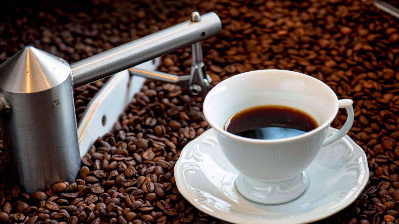xícara de porcelana branca com café coado sobre grãos de café postos em um torrador
