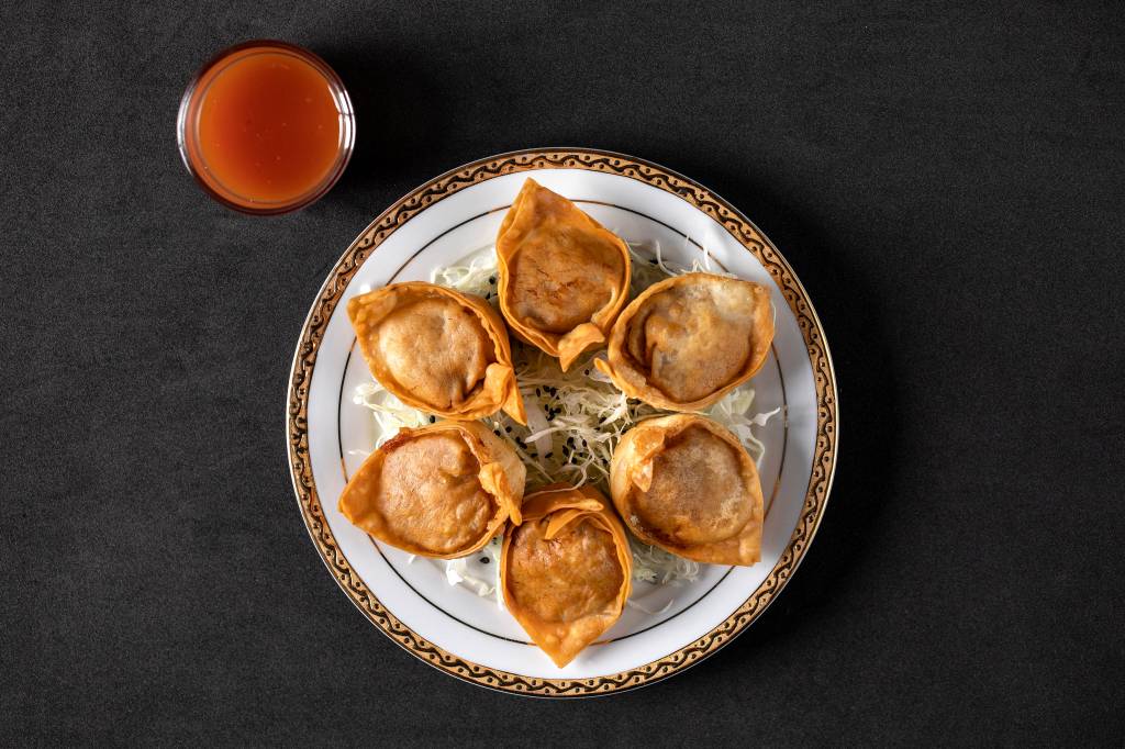 Wantan de porco frito e vegetais_Tan Tan_Tati Frison Fundo preto, com pastéizinhos chineses no prato de cor branca, recheados de porco com vegetais na companhia de molho agridoce ao canto direito