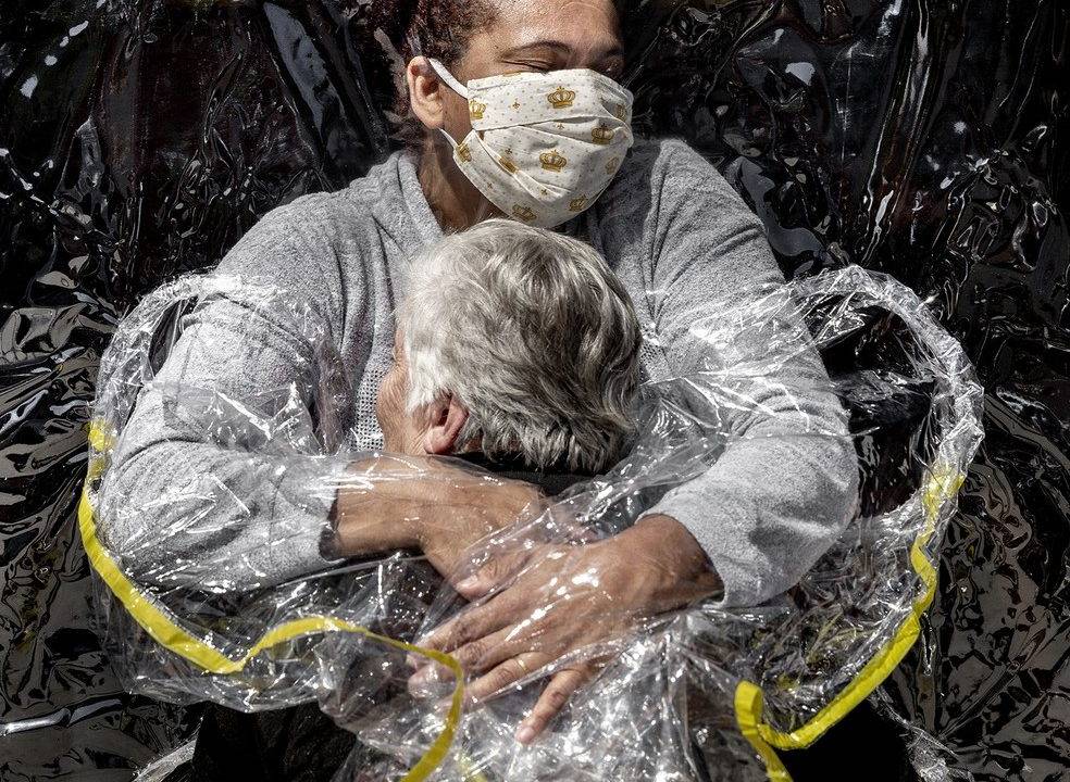 Imagem mostra enfermeira abraçando uma idosa por meio de um plástico para evitar a contaminação de Covid-19