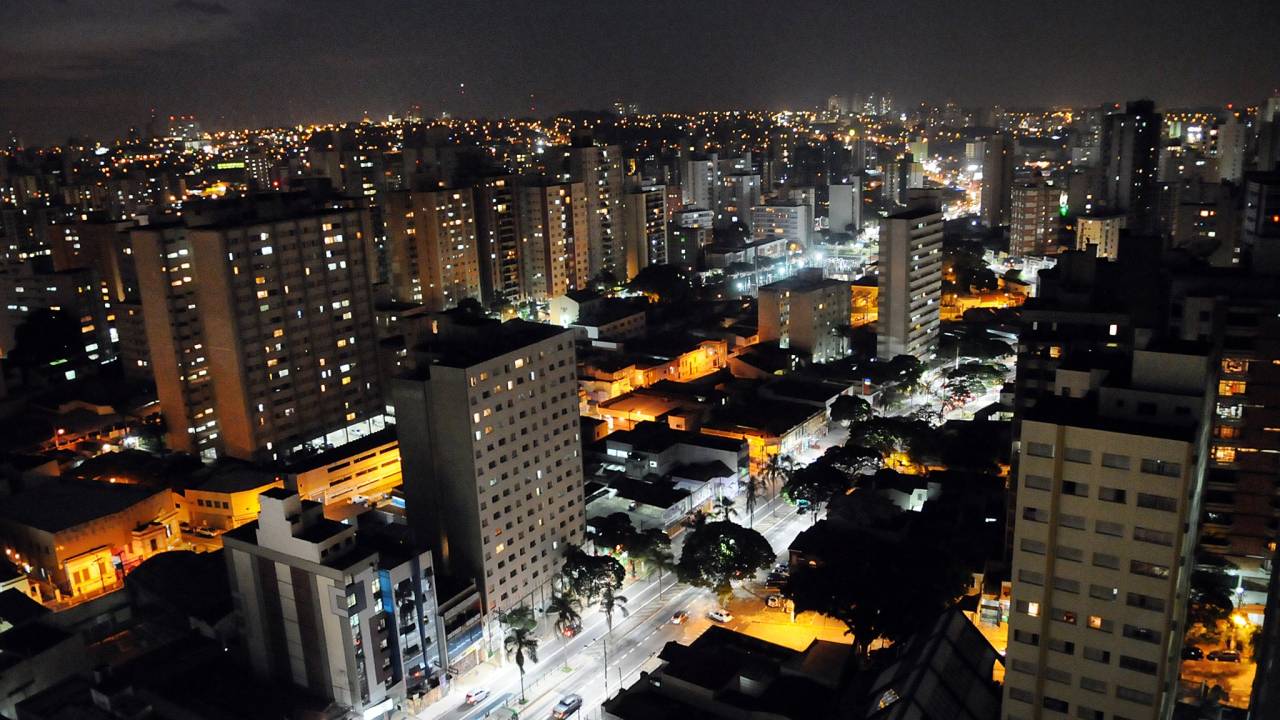 A imagem mostra a cidade de Campinas à noite, com prédios iluminados