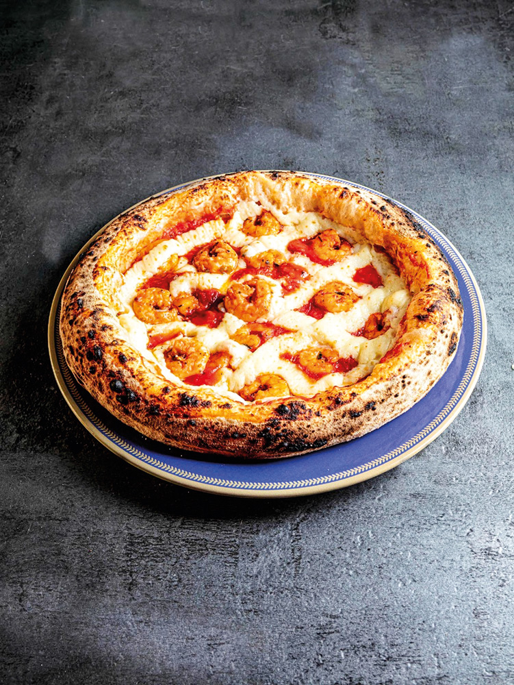 Caspita – Pizza com camarão Pizza individual com recheio de camarão, molho de tomate e catupiry sobre um balcão preto