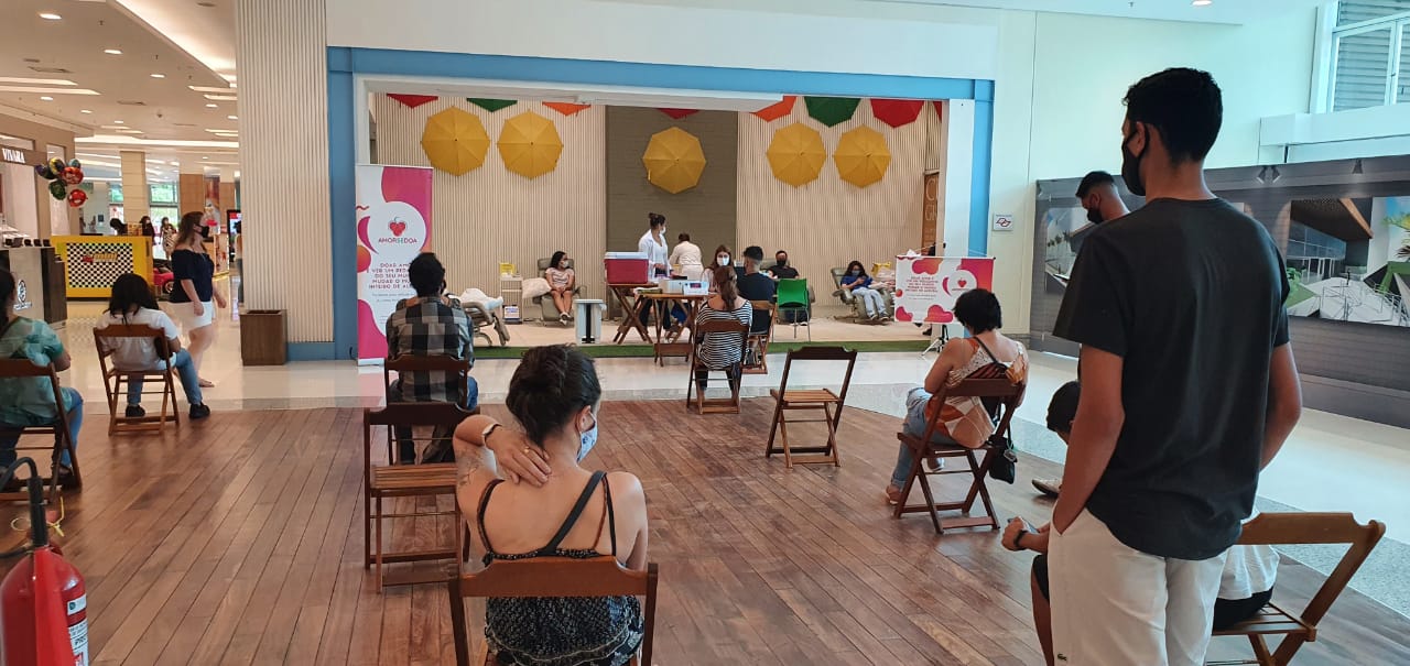 Na imagem é possível ver uma área grande do shopping, com cadeiras distanciadas e pessoas de máscaras, e mais ao fundo camas com pessoas deitadas fazendo doação de sangue acompanhadas de enfermeiros