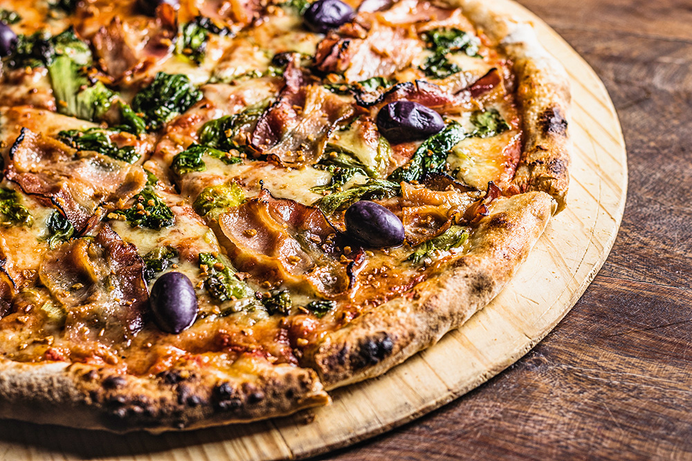 Pizza de escarola com bacon cortada em fatias sobre pá de madeira para pizzas.