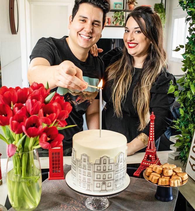 orlando e erika à frente de um bolo sorrindo para a foto enquanto ele ascende uma vela no bolo
