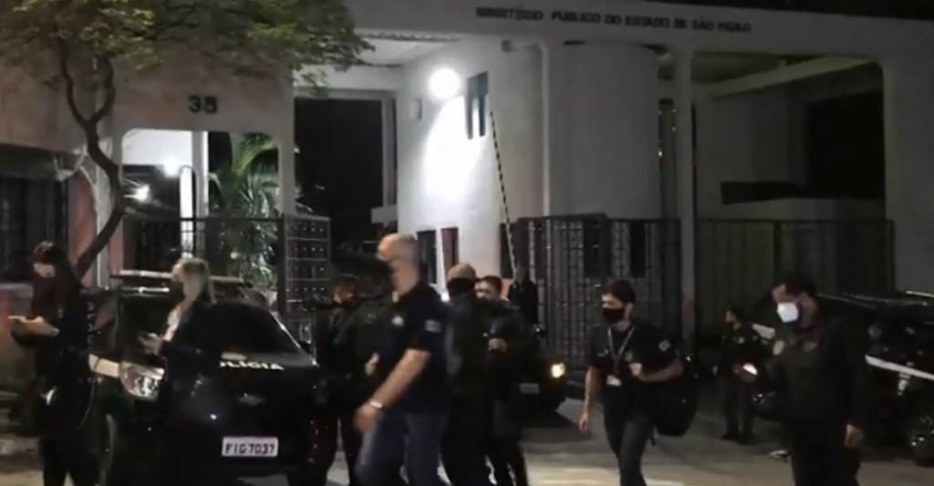 A foto ilustra a parte da frente do Ministério Público do estado de SP, com agentes e policiais na rua em frente