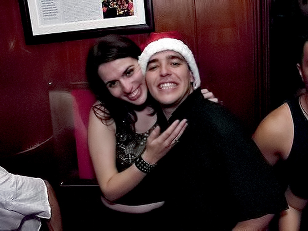 nosso-louco-amor-tentativa-homicídio-festa adriana e luciano, jovens, em uma festa, sorrindo para a foto. ele tem uma touca de papai noel