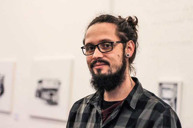 Homem de óculos e cabelo em um coque posa para foto