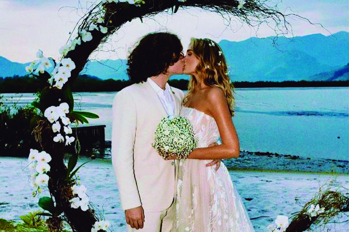 Casal João Figueiredo e Sasha Menghel se beijando no próprio casamento debaixo de portal de flores.